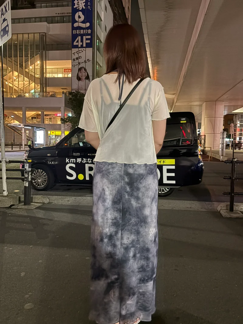 夜の街に立つあやさんの後ろ姿（ご本人）